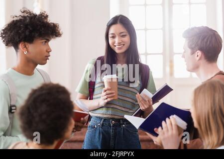 Smiling asian student with coffee and smartphone standing near multiethnic friends Stock Photo