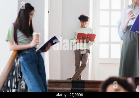 African american student holding notebook near blurred people on blurred foreground Stock Photo