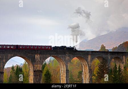 Glenfinnan, Lochaber, UK. 26th April 2021. Jacobite Steam Train first trip of 2021 with delayed steam until threequarters across the bridge. Dreich weather for the first journey across the famous Glenfinnan Viaduct with persistent rain and clouds. The train would normally begin it tourist trips on the West Highland Line in March but delayed due to Covid-19 restrictions.  . Stock Photo