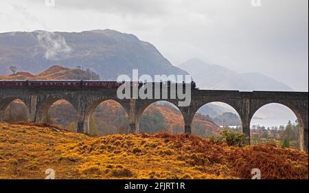 Glenfinnan, Lochaber, UK. 26th April 2021. Jacobite Steam Train first trip of 2021 with delayed steam until threequarters across the bridge. Dreich weather for the first journey across the famous Glenfinnan Viaduct with persistent rain and clouds. The train would normally begin it tourist trips on the West Highland Line in March but delayed due to Covid-19 restrictions.  . Stock Photo