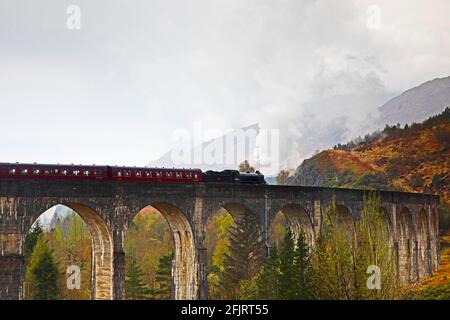 Glenfinnan, Lochaber, UK. 26th April 2021. Jacobite Steam Train first trip of 2021 with delayed steam until threequarters across the bridge. Dreich weather for the first journey across the famous Glenfinnan Viaduct with persistent rain and clouds. The train would normally begin it tourist trips on the West Highland Line in March but delayed due to Covid-19 restrictions.  . Stock Photo