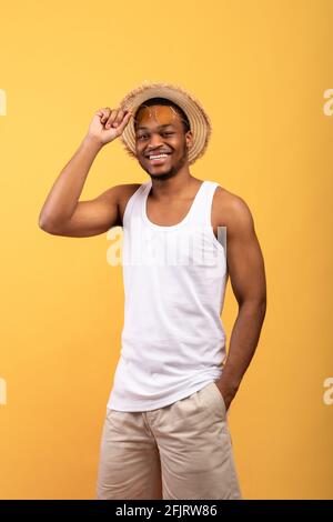 Summer vibes. Portrait of young black guy in t-shirt, shorts, straw hat and sunglasses posing and smiling at camera Stock Photo