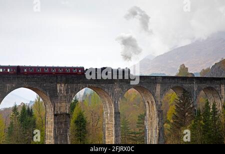 Glenfinnan, Lochaber, UK. 26th April 2021. Jacobite Steam Train first trip of 2021 with delayed steam until threequarters across the bridge. Dreich weather for the first journey across the famous Glenfinnan Viaduct with persistent rain and clouds. The train would normally begin it tourist trips on the West Highland Line in March but delayed due to Covid-19 restrictions.  . Stock Photo