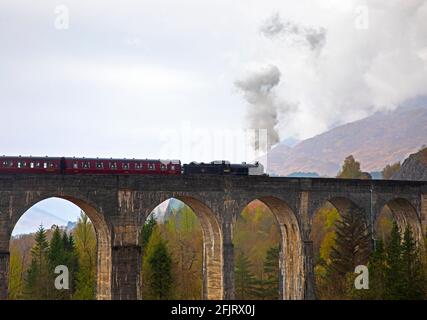 Glenfinnan, Lochaber, UK. 26th April 2021. Jacobite Steam Train first trip of 2021 with delayed steam until threequarters across the bridge. Dreich weather for the first journey across the famous Glenfinnan Viaduct with persistent rain and clouds. The train would normally begin it tourist trips on the West Highland Line in March but delayed due to Covid-19 restrictions.  . Stock Photo