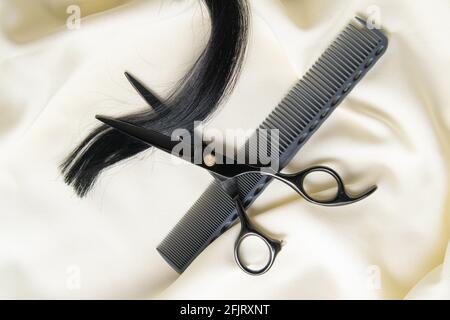Lock of black hair ready for trim with comb and scissors. The hair is waving left to right and goes through the black comb. The scissors are laying on Stock Photo