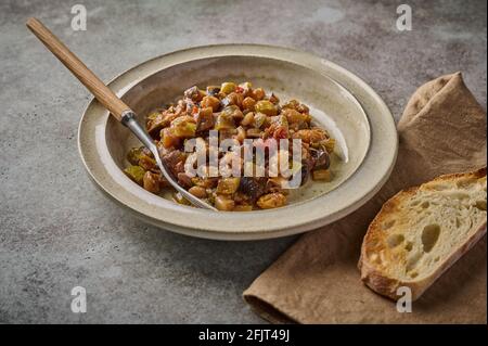 Homemade traditional Sicilian caponata with eggplant, zucchini, tomatoes, olives and ciabatta bread. Close up, copy space Stock Photo