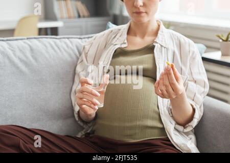 Close-up of pregnant woman sitting on sofa drinking water with vitamin in the room Stock Photo