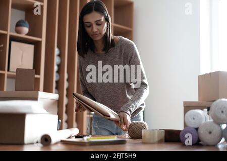 delivery, mail service, shipment concept - Indian mixed-race woman packing eco parcel box and tying rope at post office. Stock Photo