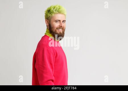 Profile of cheerful bearded Caucasian man has happy expression smiles broadly, has white perfect teeth, wears red sweater, looks at camera. Copy space Stock Photo