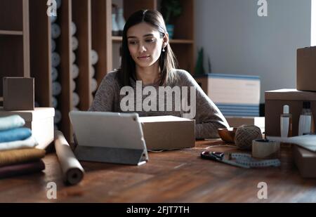 Indian mixed-race female seller using tablet checking ecommerce clothing store orders Stock Photo
