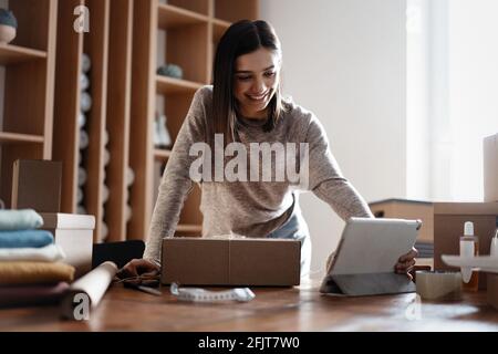 Indian mixed-race female seller using tablet checking ecommerce clothing store orders Stock Photo