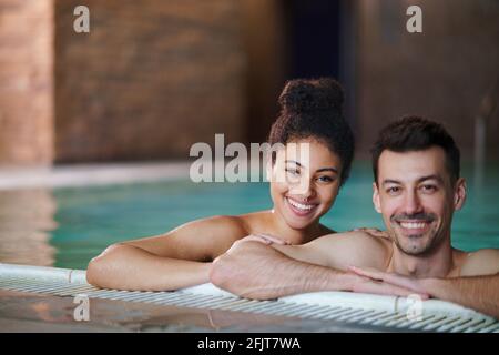 Portrait of young couple in swimming pool, looking at camera. Stock Photo