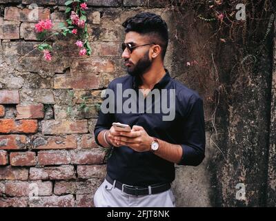 Handsome Indian man wearing a black shirt and sunglasses and holding a phone Stock Photo