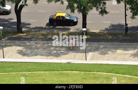 one of the streets and parks of Buenos Aires, with a taxi circulating and a woman on a bicycle walking through the Palermo neighborhood on a sunny Sat Stock Photo