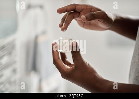 African man taking cream out of a jar with his finger Stock Photo