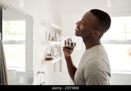 Smiling young African man spraying on cologne in his bathroom Stock Photo