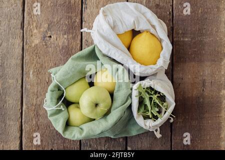 Fresh apples, lemons and arugula in eco cotton bags on rustic wooden table. Zero waste. Plastic free grocery shopping. Organic fruits and vegetables i Stock Photo