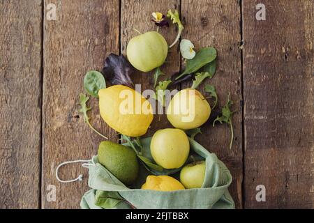 Eco friendly zero waste shopping concept. Fresh apples, lemon, avocado, salad leaves scattered from eco cotton bag on rustic wood. Salad ingredients. Stock Photo