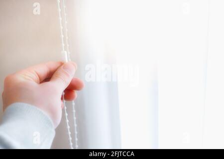A man closes the blinds on the windows from the sunlight. Advertising photo for the manufacturer of blinds with space to copy. Soft focus Stock Photo