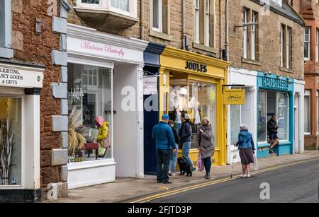 North Berwick, East Lothian, Scotland, United Kingdom, 26th April. Businesses reopen: with lockdown restrictions eased today, shops are open. Pictured: People wearing face masks queue outside a Joules shop in the High Street. Stock Photo