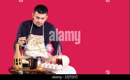 Banner, long format on red background. The male chef in the kitchen opens the pan. Steam is coming out of the pot from table with food products. Man Stock Photo