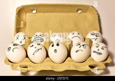 Chicken eggs in a cardboard box with painted emotions on the shell. Egg with a face of sadness, depression and fear. Stock Photo