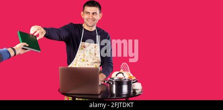 Banner, long format on red background. Man sitting at the laptop on the kitchen table, receive record recipe book for writing in notepad handwritten Stock Photo