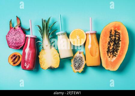 Assortment of colorful smoothie drinks in glass bottle with straw and fruit ingredients - papaya, orange, pineapple, dragon fruit, pitahaya, tamarillo Stock Photo