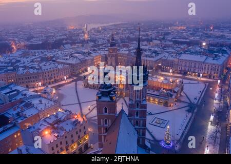 Main square Rynek of the Old Town of Krakow Poland in winter. St. Mary's Basilica Gothic church and Krakow Cloth Hall, covered in snow at evening with Stock Photo