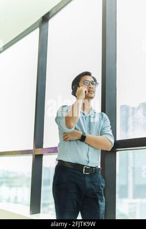 Businessman standing next to big window inside modern building talking on cell phone. Stock Photo