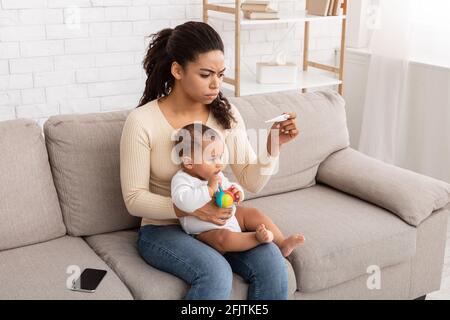 Black Mom Measuring Temperature For Sick Baby Having Fever Indoor Stock Photo