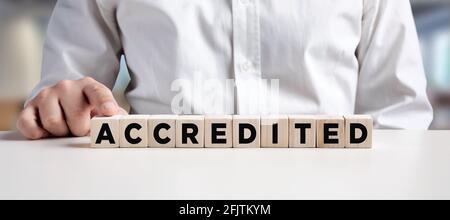 Businessman pressing his finger on the wooden cubes with the word accredited. Business industry standards concept. Stock Photo