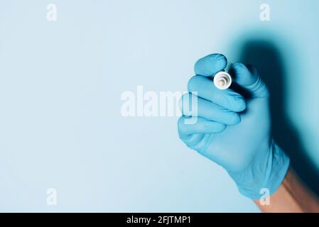 Woman's hand in medical gloves holding marker on blue background. Copy space. Coronavirus, COVID-19 pandemic. Quarantine end concept. Stay safe Stock Photo