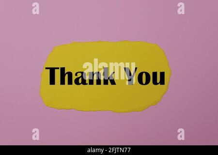 Thank you written on a yellow torn paper on a pink background. Stock Photo