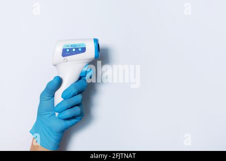 Hand in medical glove with digital infrared non contact thermometer gun for measuring temperature on white background for coronavirus COVID-19 testing Stock Photo