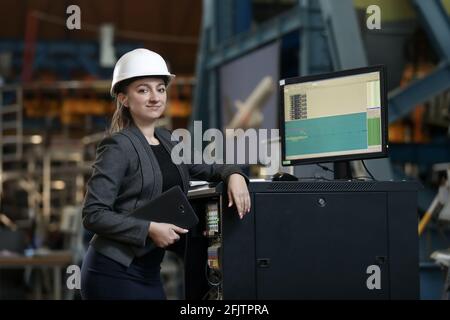 Portrait of a female factory manager in a white hard hat and business suit. Controlling the work process at the airplane manufacturer. .  Stock Photo