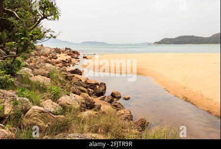 A small waterway, which separates small sand dune and rocks, ends at the sea. Stock Photo
