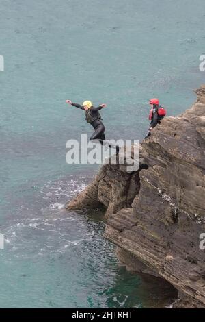A holidaymaker leaping from rocks during a coasteering session around the inter tidal zone at Towan Head in Newquay in Cornwall. Stock Photo