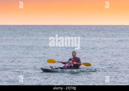 A holidaymaker and his young daughter on a GoSea Sit-on-Top kayak in the sea in evening light at Little Fistral in Newquay in Cornwall. Stock Photo