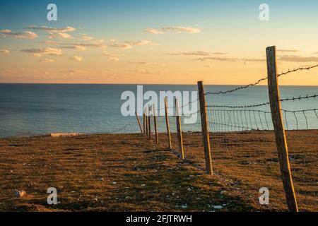 A barbed wire fence lit by evening sunlight on the edge of the cliffs on Rough Brow (3) Stock Photo