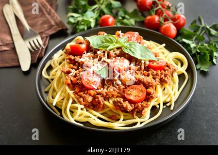 Tasty spaghetti with minced meat, cherry tomatoes and parmesan cheese on black stone background Stock Photo