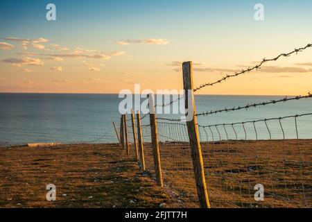 A barbed wire fence lit by evening sunlight on the edge of the cliffs on Rough Brow (2) Stock Photo