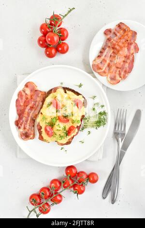 Scrambled eggs with microgreen, bacon and tomato slices on bread. Top view, flat lay Stock Photo