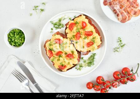 Scrambled eggs with microgreen, bacon and tomatoes on bread. Top view, flat lay Stock Photo