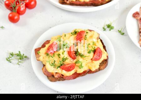 Scrambled eggs with microgreen, bacon and tomato slices on bread, close up Stock Photo