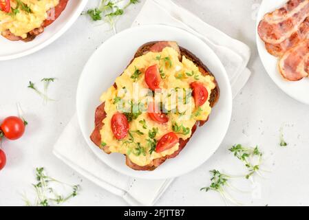 Scrambled eggs with microgreen, bacon and tomatoes on bread. Top view, flat lay Stock Photo