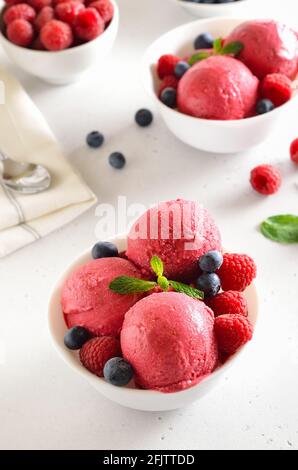 Raspberry ice cream scoop with fresh raspberries and blueberries in bowl on stone background. Cold summer dessert Stock Photo