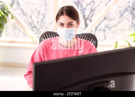 Shot of beautiful woman wearing face mask while sitting behind her computer and working. Home office. Stock Photo