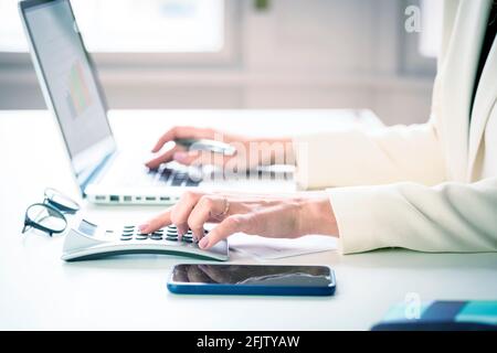 Close-up shot of unrecognizable financial analyst businesswoman using calculator and laptop while working on business plan. Stock Photo