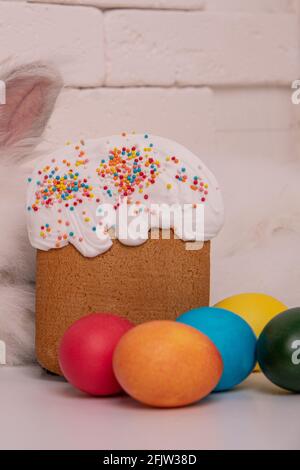 Easter cake and colorful eggs of different colors lie around in the foreground. Brickwork in the background. Easter bunny ear Stock Photo